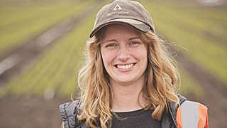 Smiling woman wearing Weyerhaeuser baseball cap in foreground of field of newly planted trees.