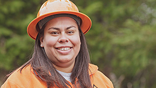 Smiling woman wearing hardhat in foreground of forest.